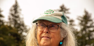 An elder with glasses, long white hair and a green hat.