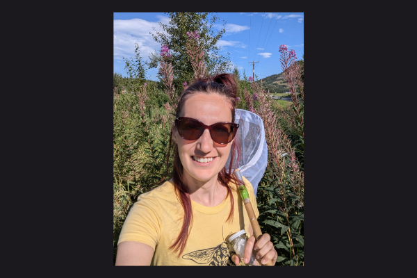 A woman stands outside with a bug capturing net. 