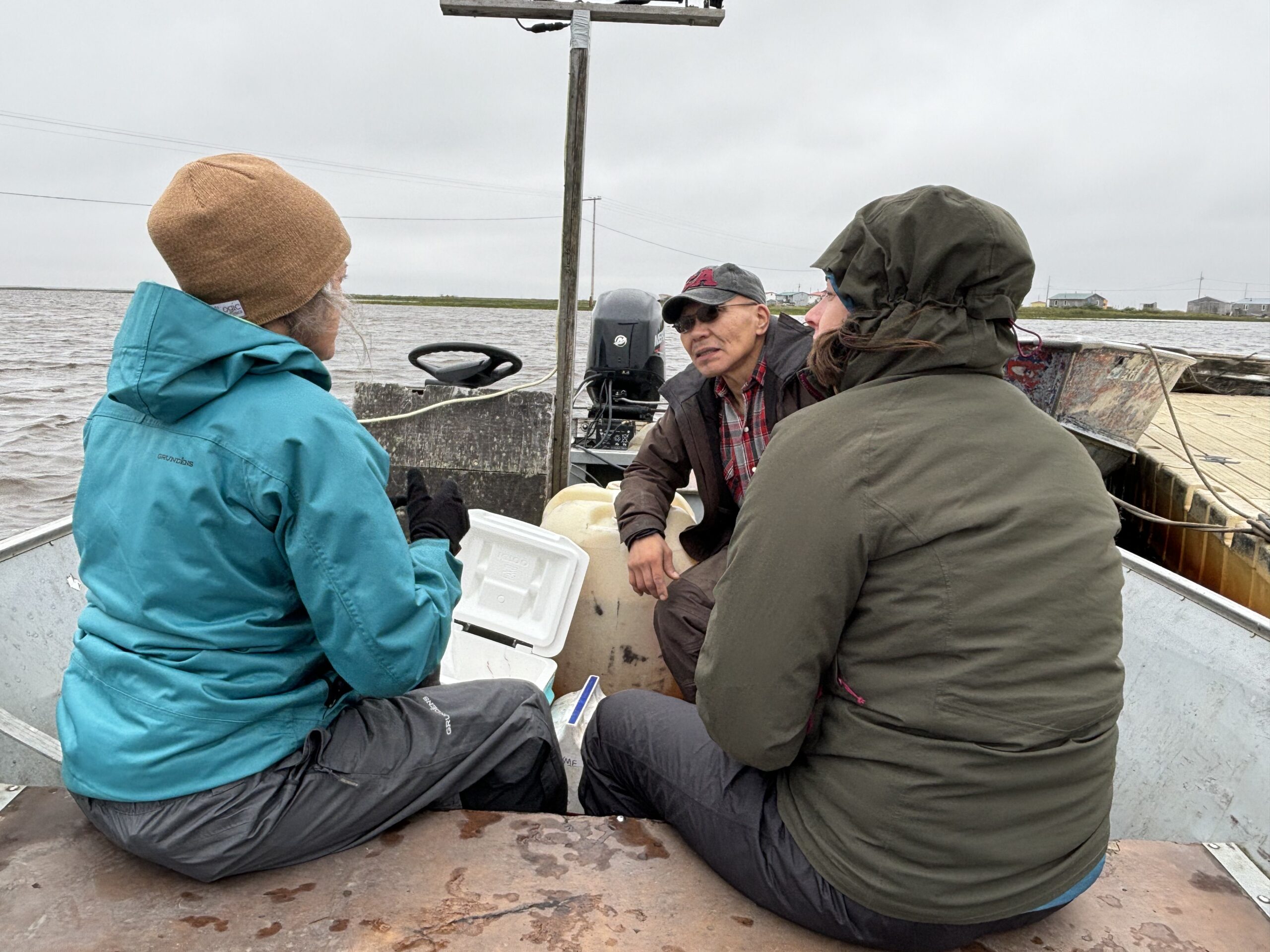 Three group wearing rainfall jackets beryllium successful a boat, facing each different and talking.