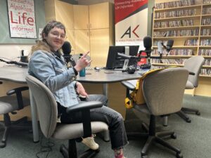 A woman sits in a radio studio giving the devil horns. 