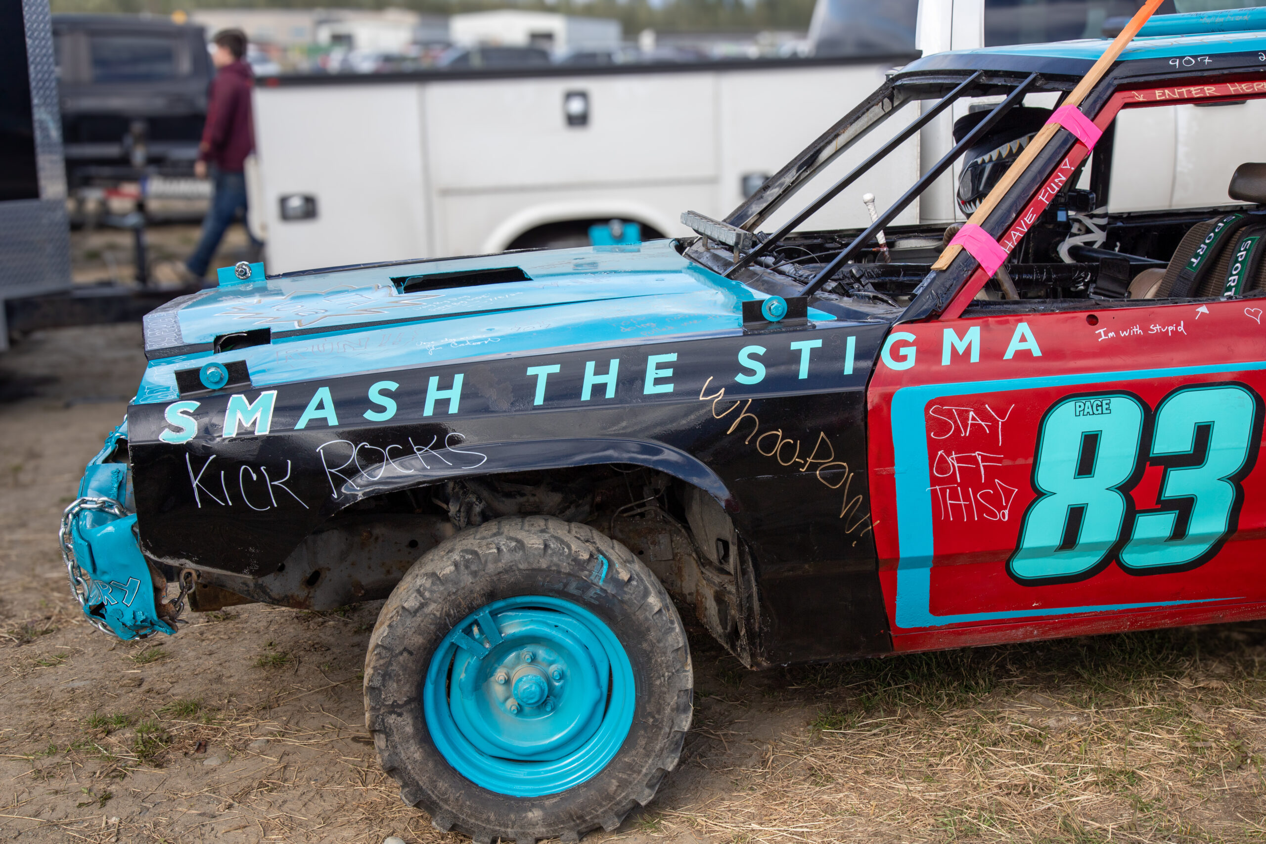 a car is painted with black and bright blue, with one red door. it says smash the stigma in block letters and is tagged with handwritten messages like "KICK ROCKS" and "have fun!"