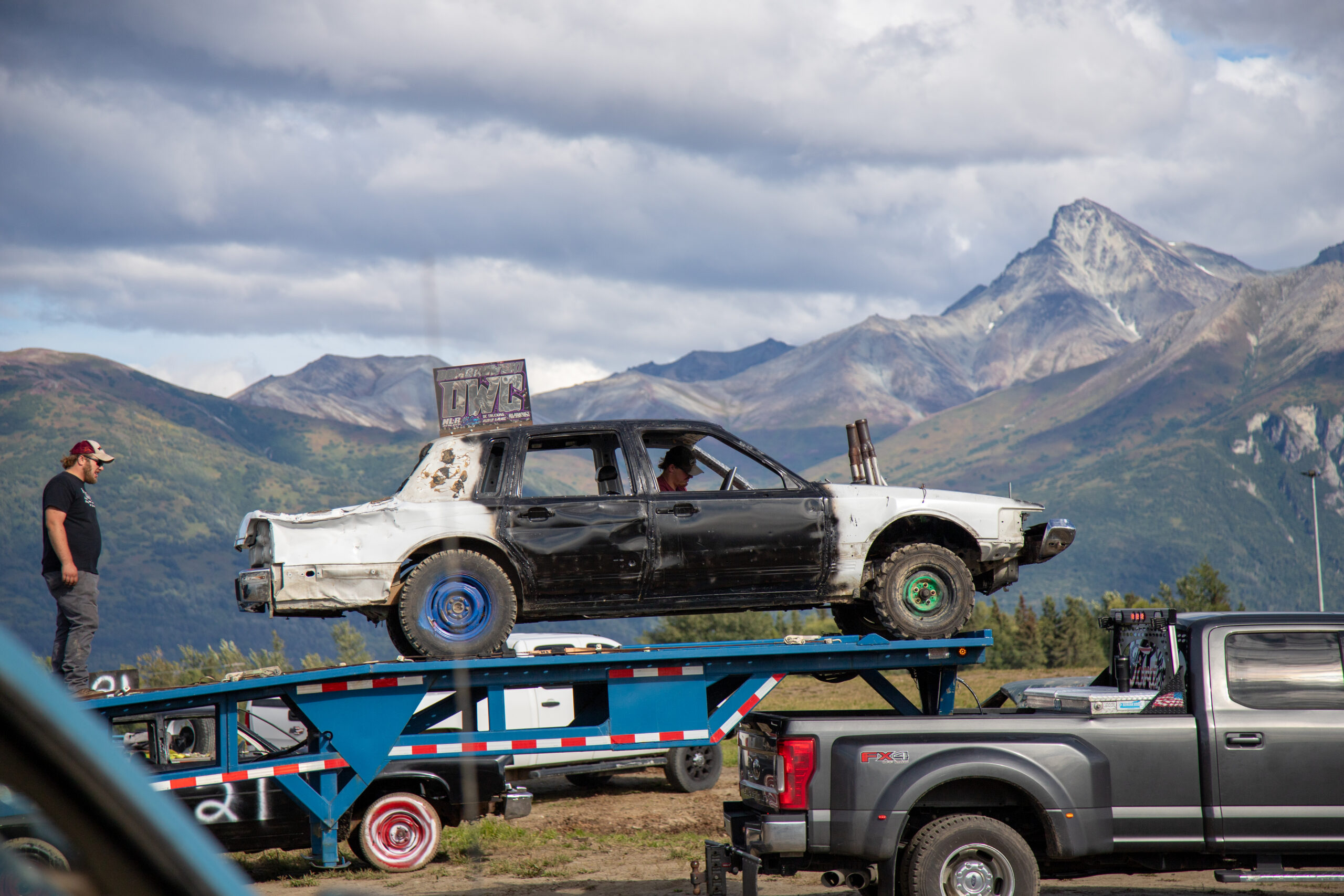 a old car half painted white and half painted black has been towed it. in the background are mountians