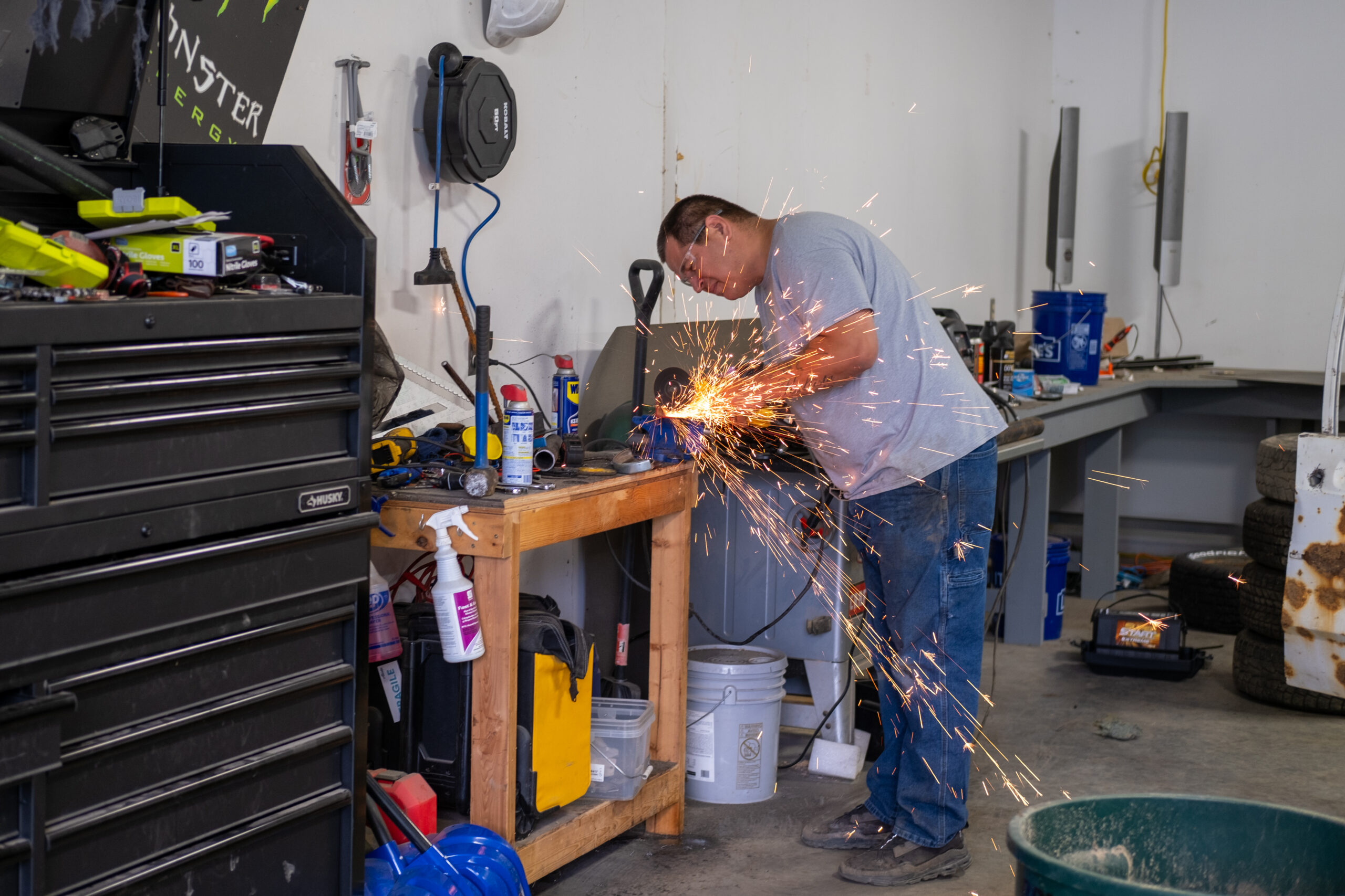 a man leans over a work bench where orange sparks fly around his hand