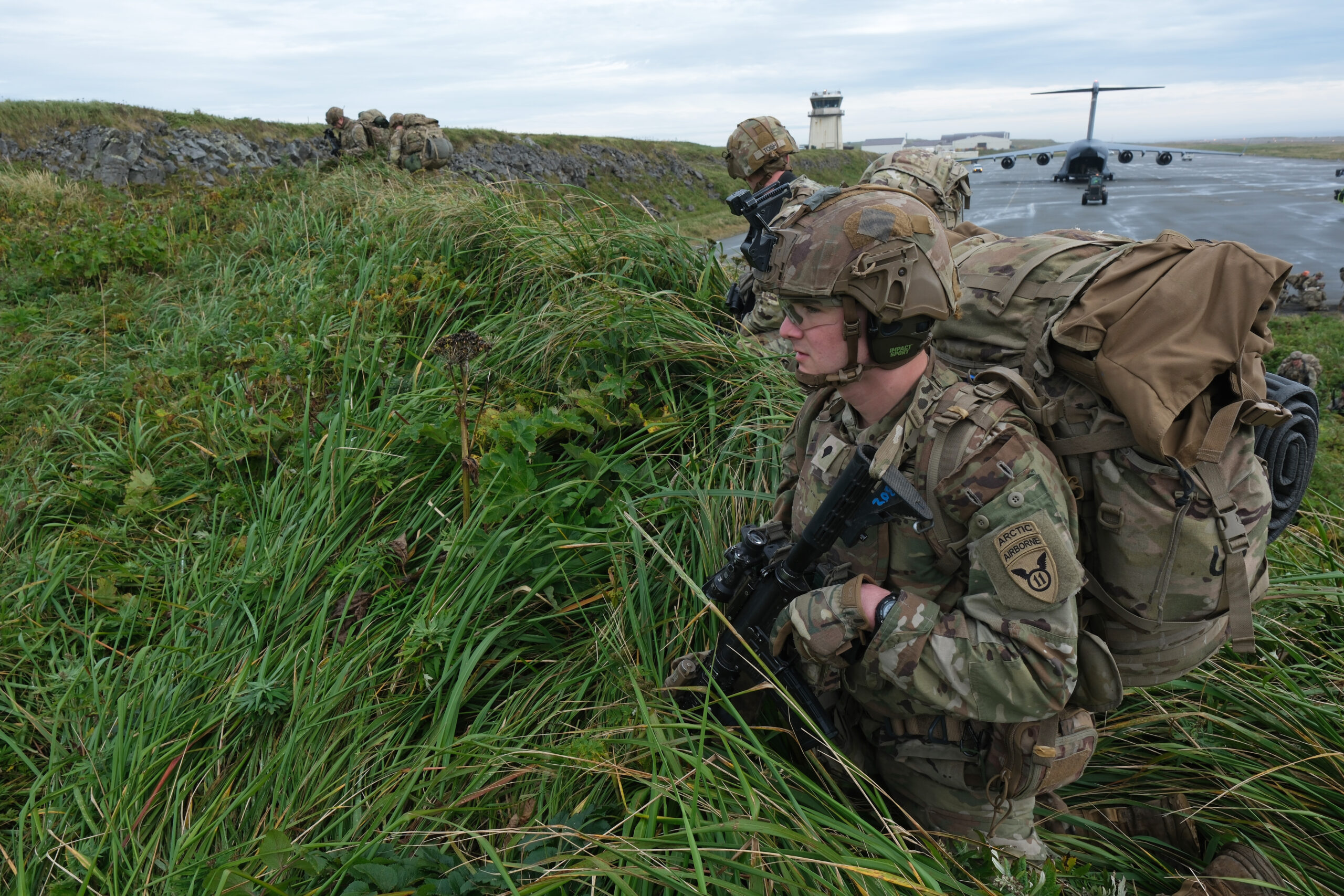 Men in military uniforms stand in tall grass.