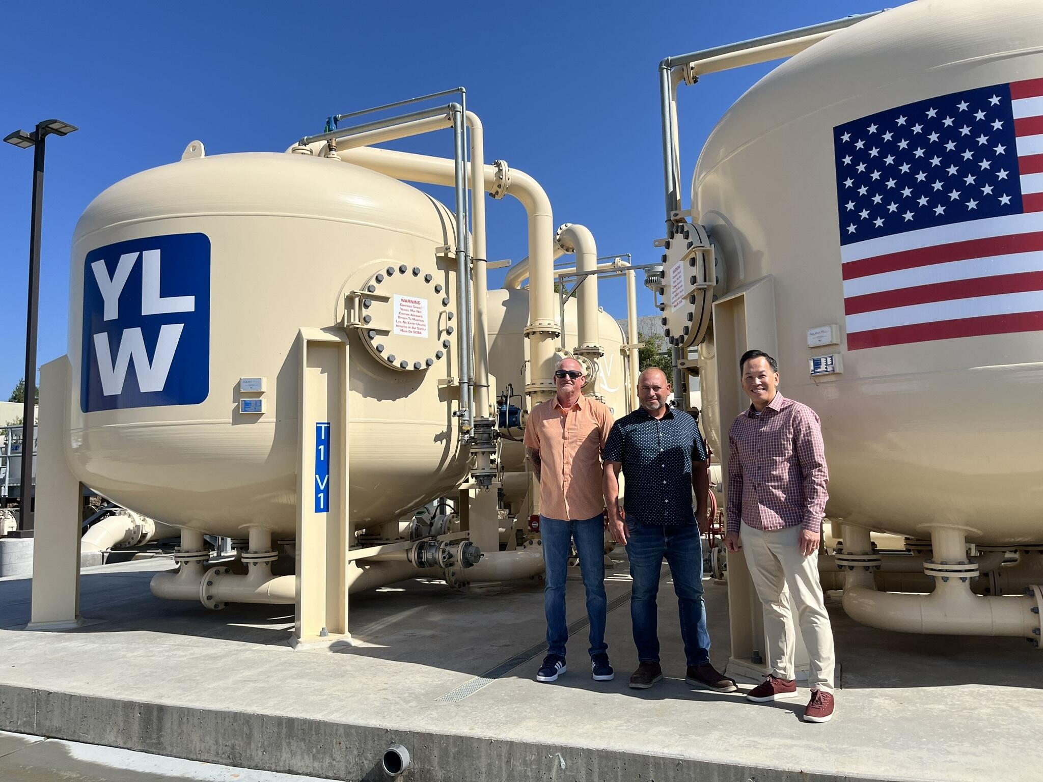 three people stand next to giant vats of water