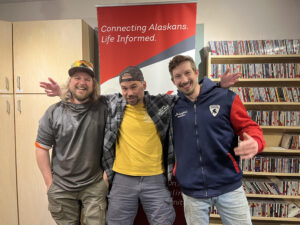 Three guys pose in front of a sign. 