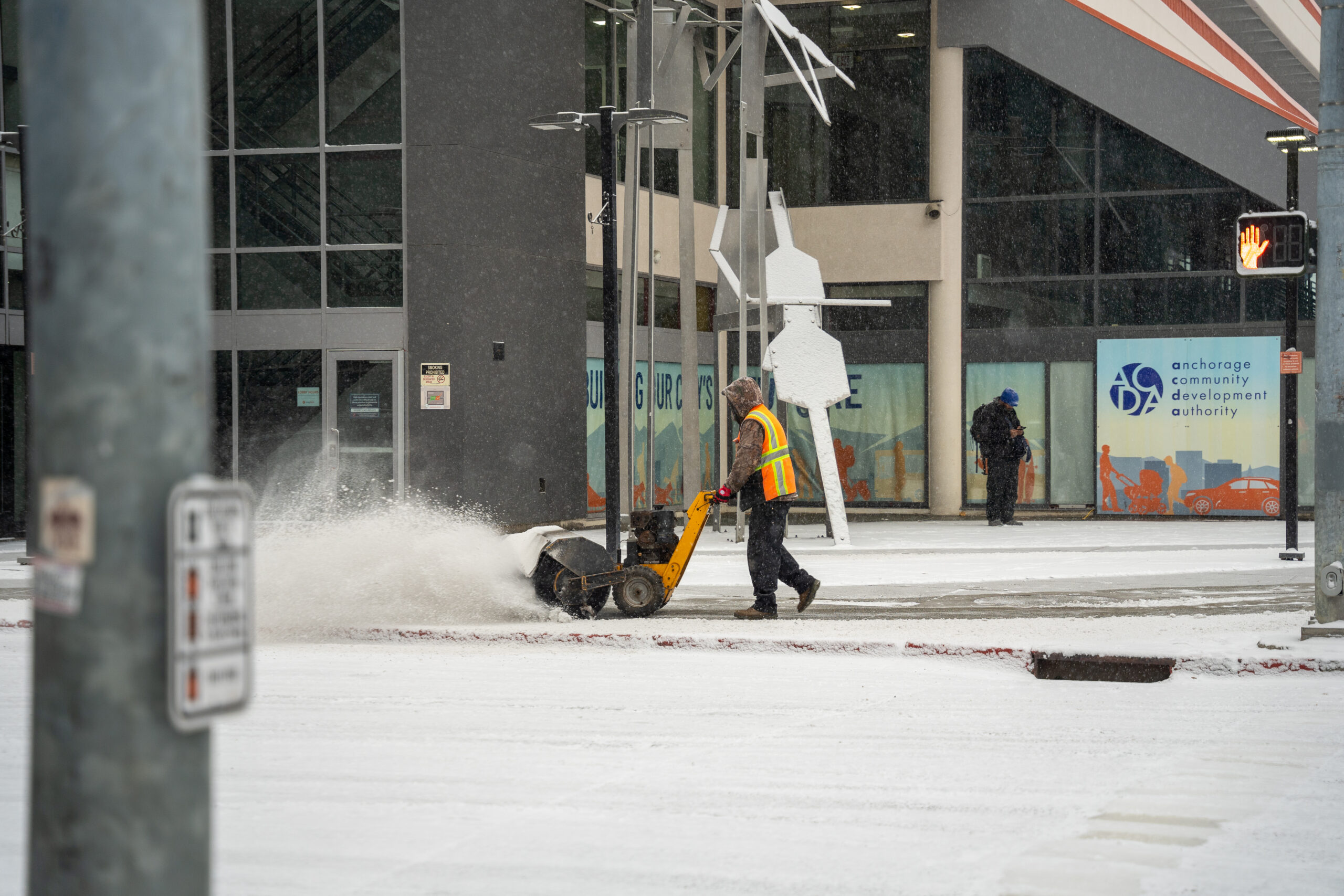 A man snow blowing the side walk.