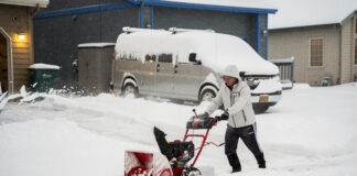 A man snow blowing his driveway.