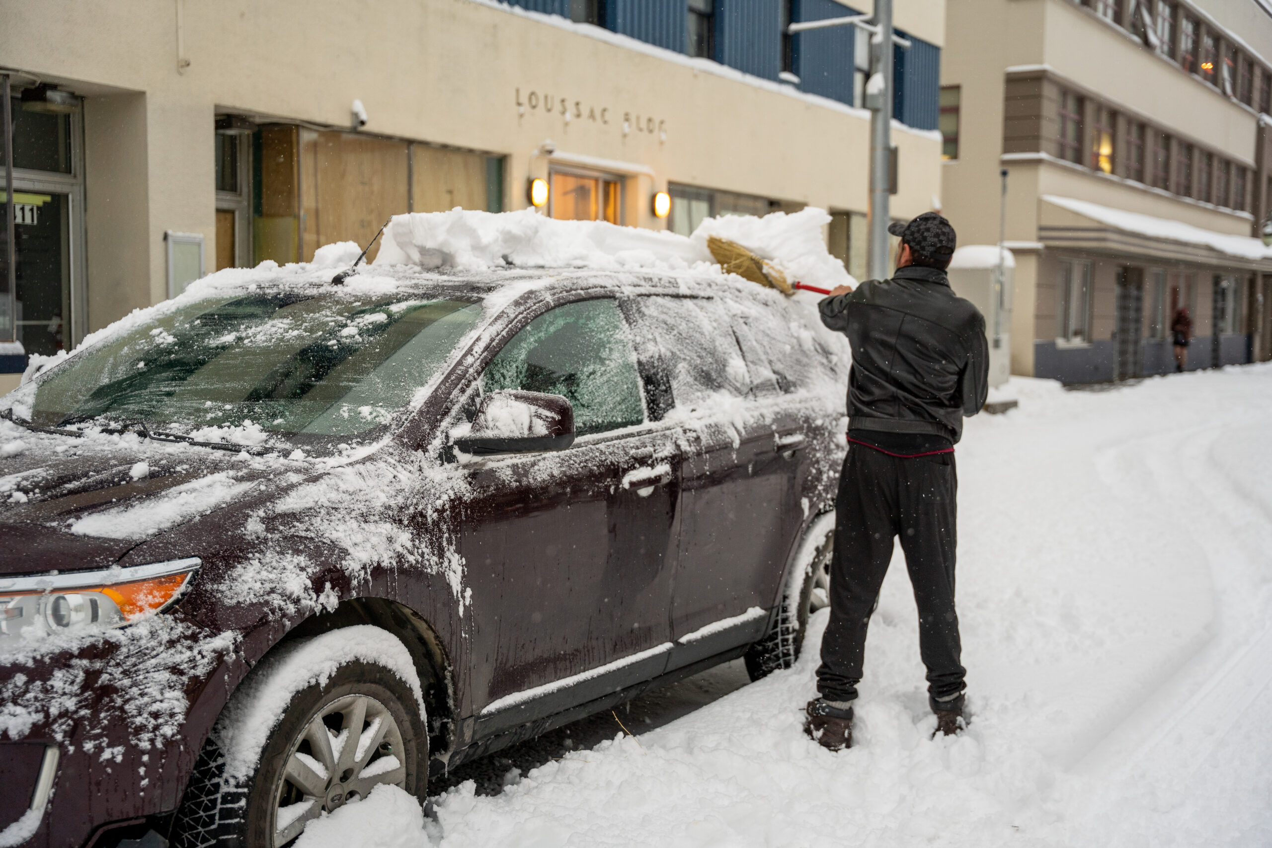 A man with a broom cleaning off snow of his car.