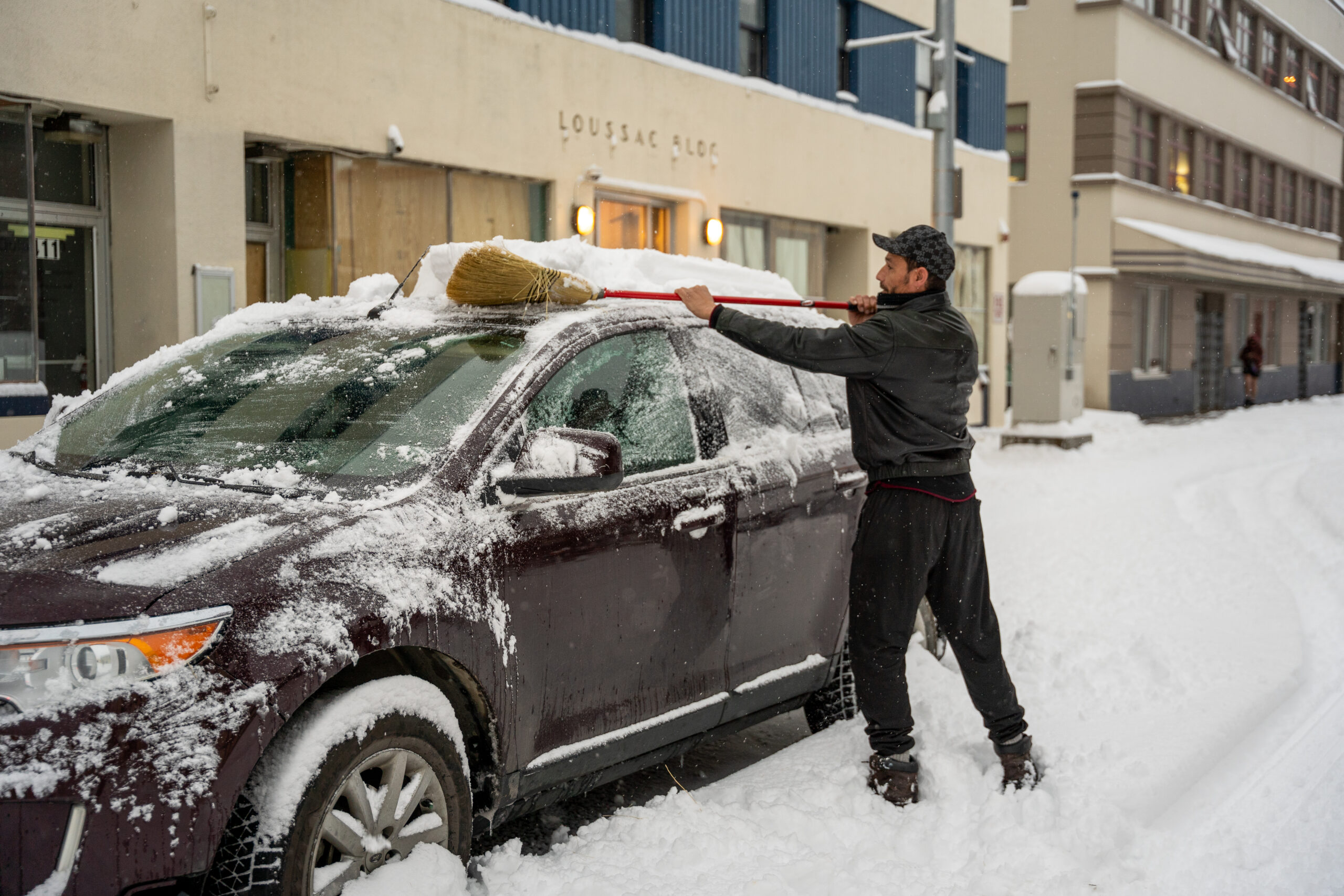 A man with a broom cleaning off snow of his car.