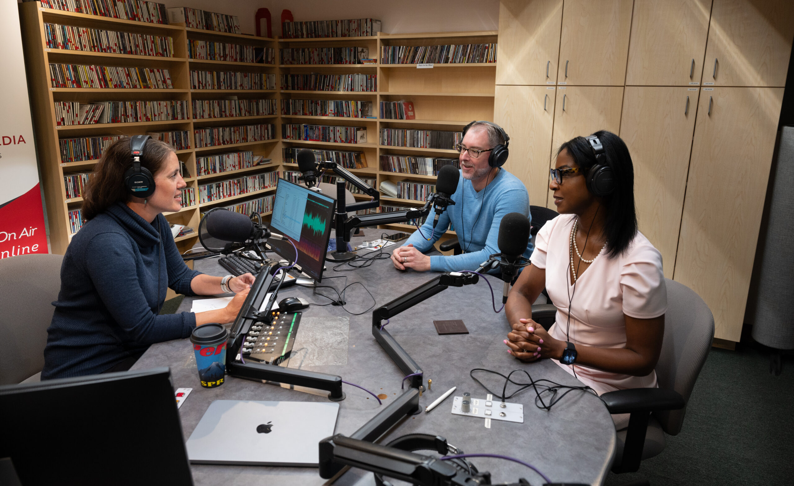 Three people speak to each other in a radio studio.