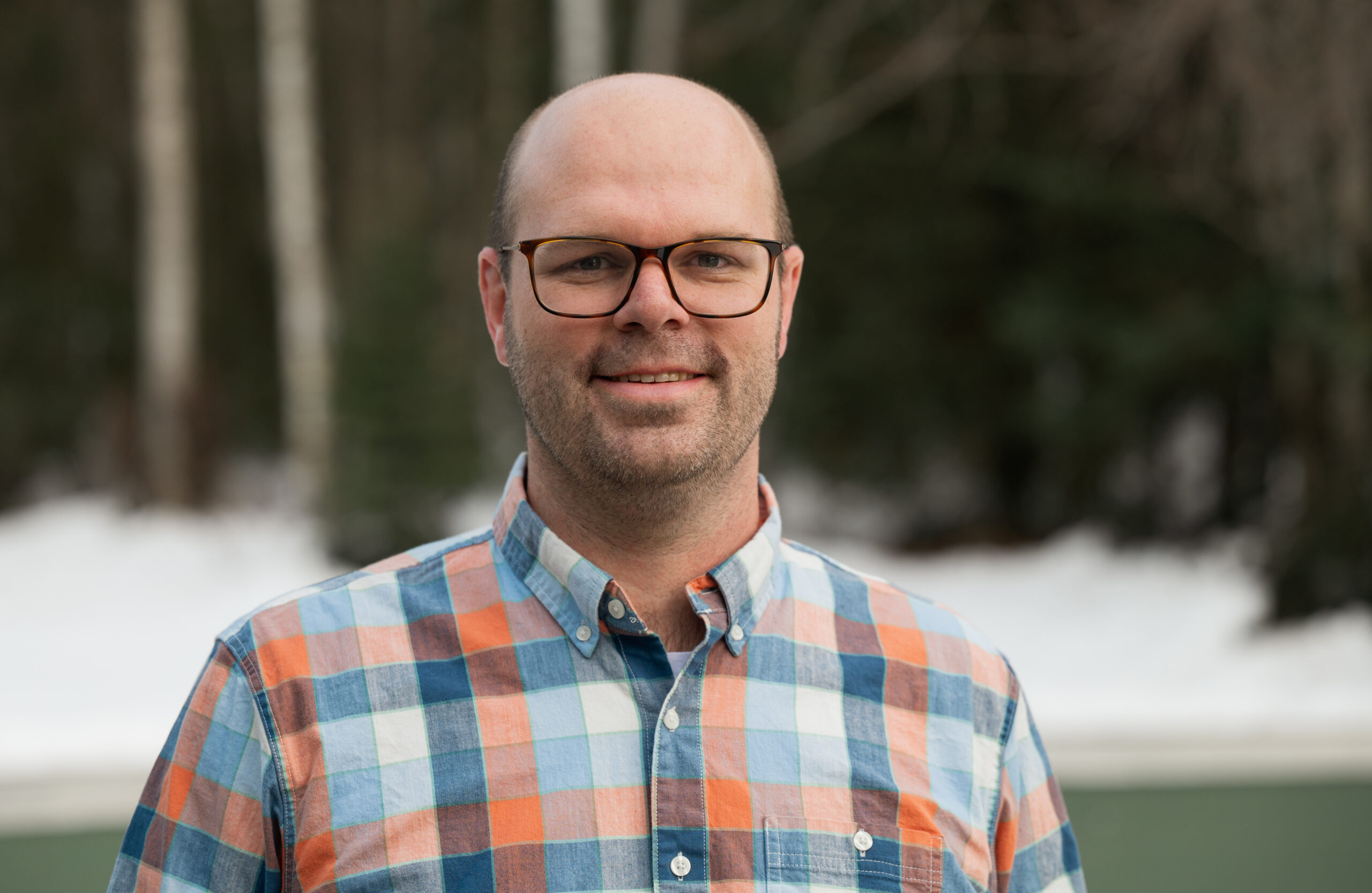 A man in a plaid blue and orange shirt stands outside.