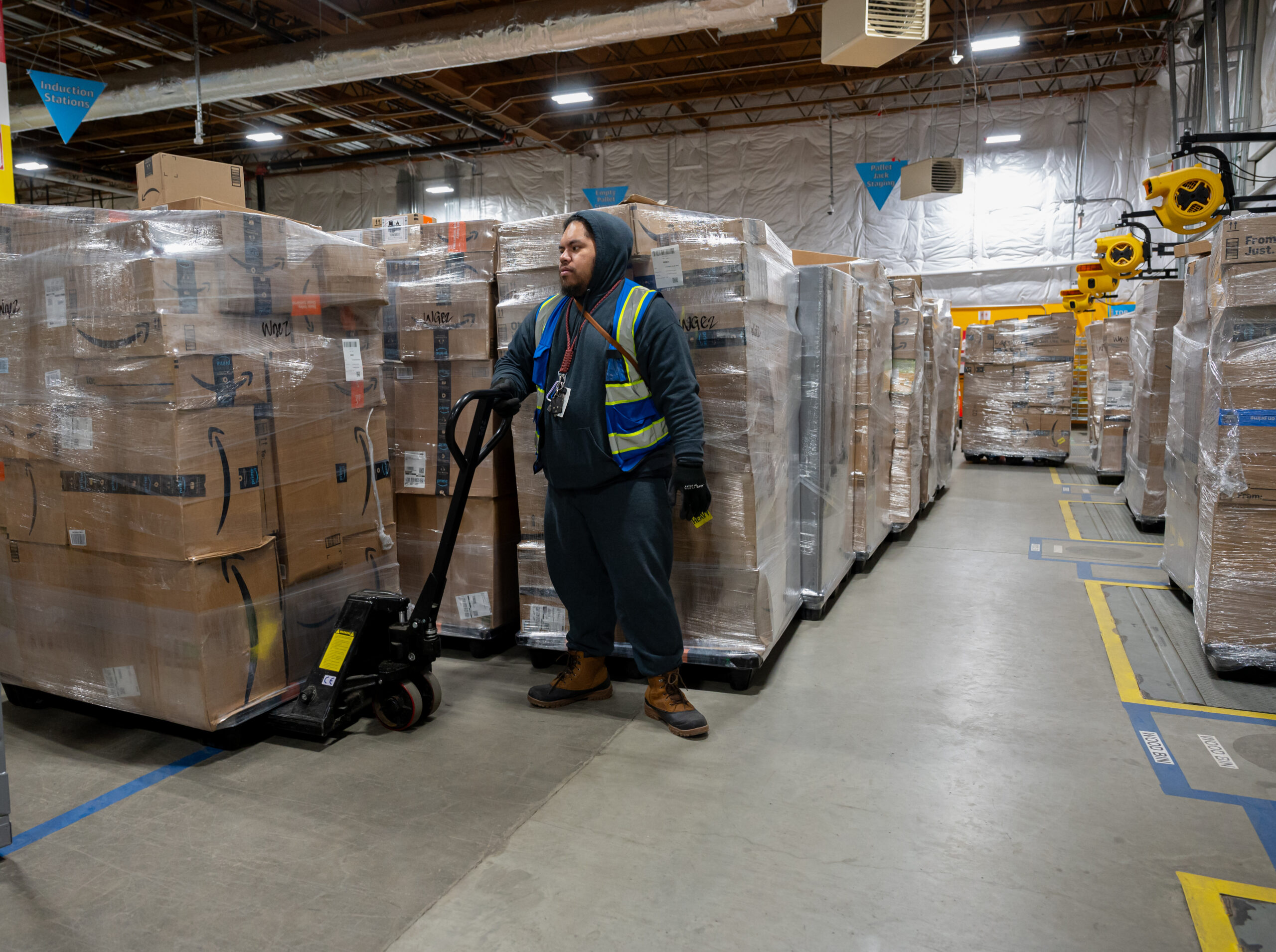 A man standing next to a tall pallet of Amazon packages.