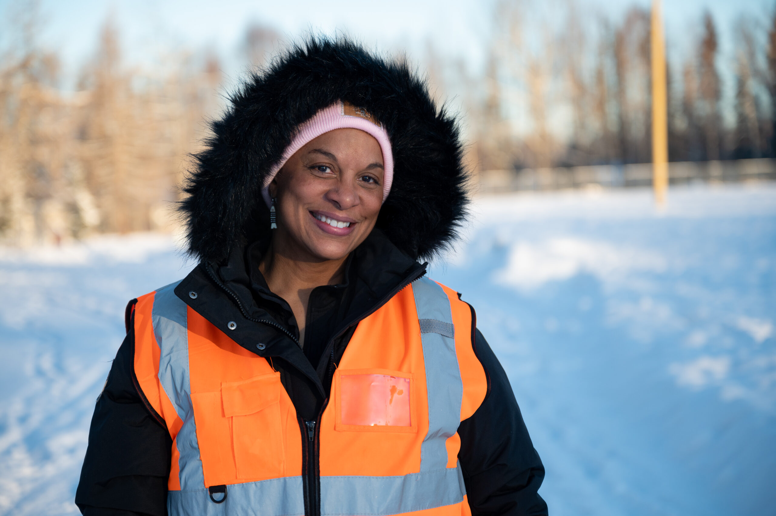 A woman in a black coat and orange safety vest.