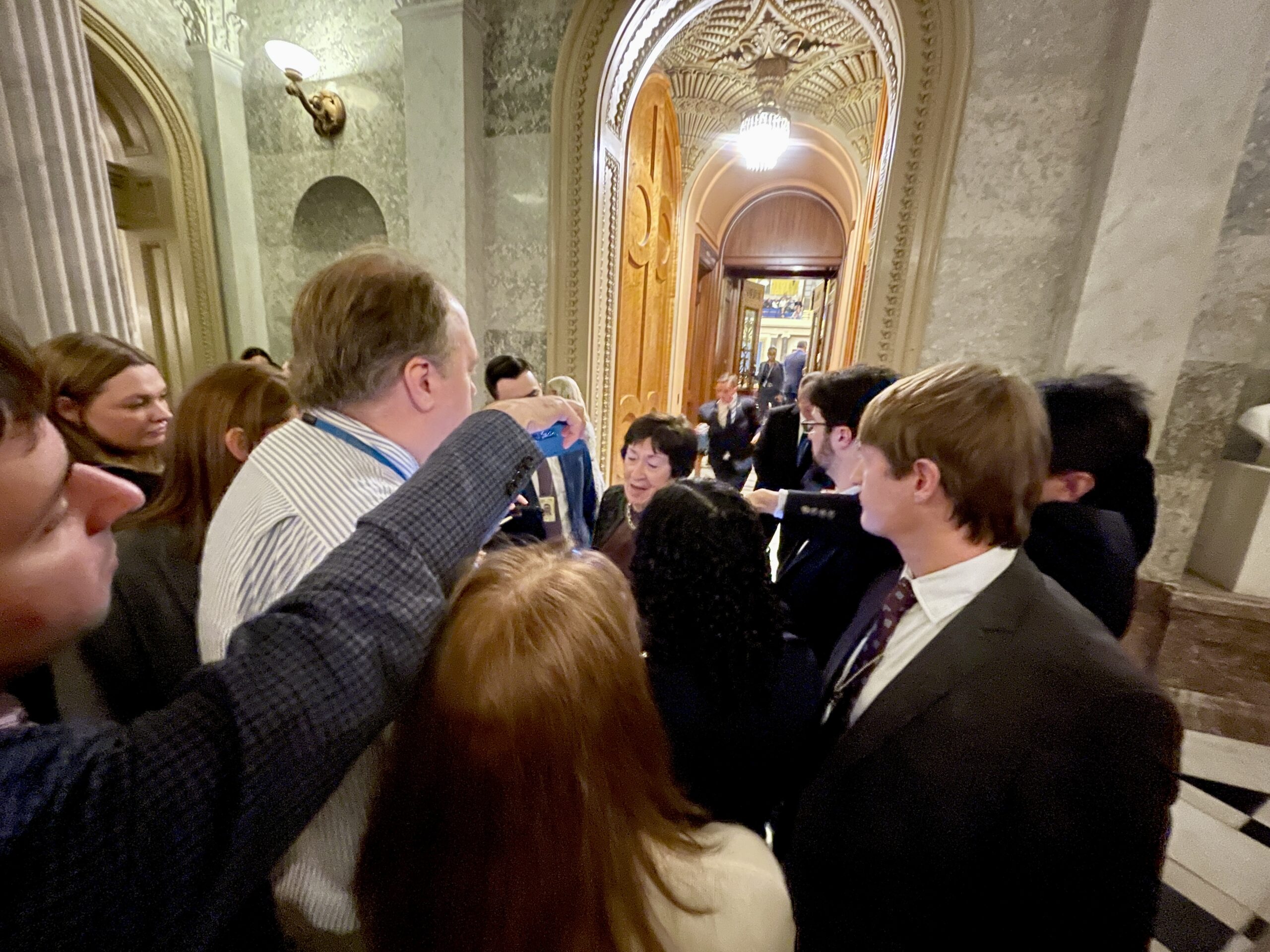 crowd of people in a grandiose building, surrounding a small figure