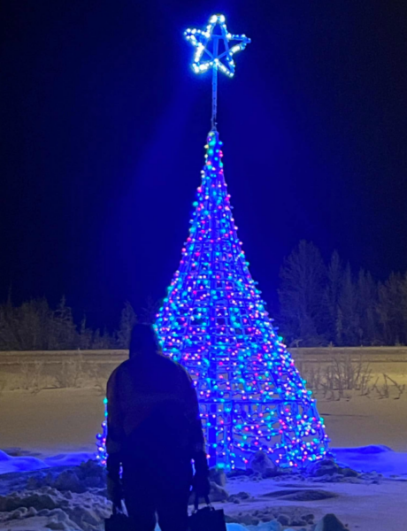 A man walks through the snow to a multi-colored lit Christmas Tree.